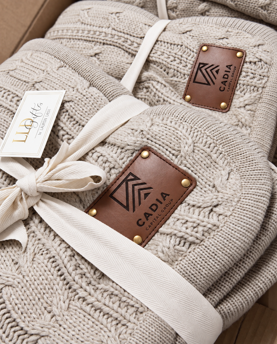 Cream cable-knit corporate blankets with engraved company-logo patches and ivory ribbon
