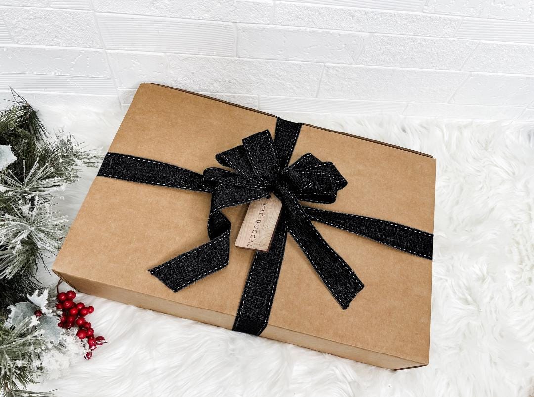 A brown cardboard box with a black ribbon bow tied around it, placed on a white fur rug.