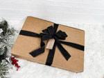 A brown cardboard box with a black ribbon bow tied around it, placed on a white fur rug.