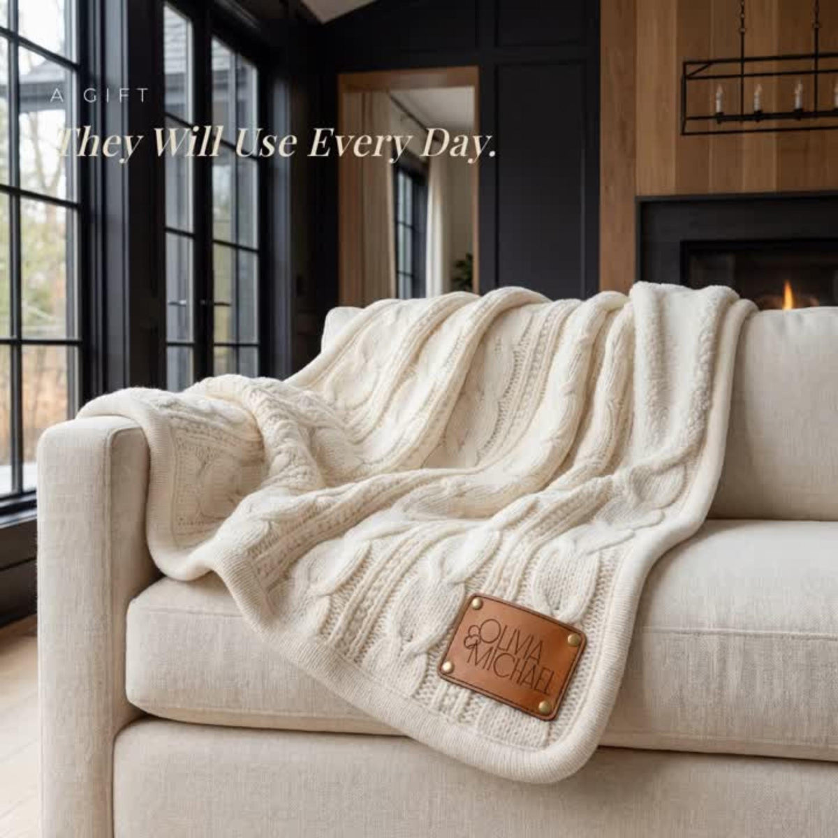 A cozy, beige knitted blanket is draped over a white couch, with a leather patch on the blanket displaying the text "Olivia Michael".