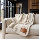 A cozy, beige knitted blanket is draped over a white couch, with a leather patch on the blanket displaying the text "Olivia Michael".